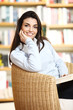 smiling female student with book in hands sitting in a chair in
