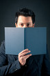 Foto: Young man behind a book against dark background. Young man behind a book against dark background.