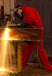 Welder in red overalls cuts metal.