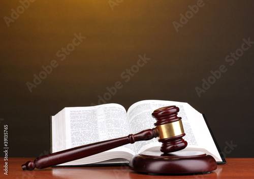 Photo: Judge's gavel and open book on wooden table on brown background Judge's gavel and open book on wooden table on brown background