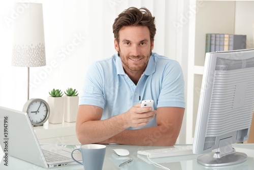 Photo: Smiling man at desk with mobile phone Smiling man at desk with mobile phone