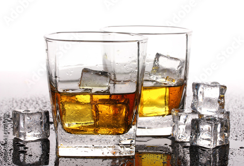 Photo: two glasses of scotch whiskey and ice on table isolated on white two glasses of scotch whiskey and ice on table isolated on white