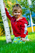 The small beautiful girl sits on a green lawn and laughs