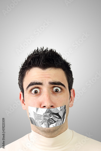 Photo: Scared young man having gray duct tape on his mouth Scared young man having gray duct tape on his mouth