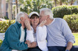 Two senior men kissing their female friend in a park