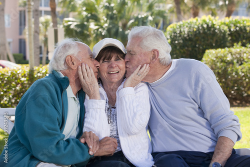 Photo: Two senior men kissing their female friend in a park Two senior men kissing their female friend in a park