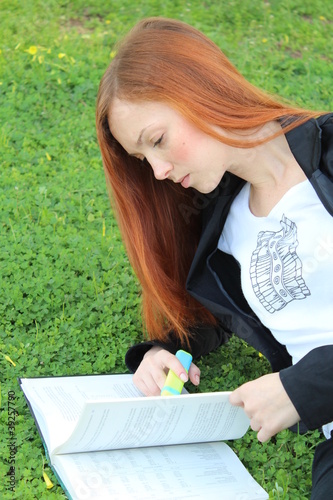 Photo: Redhead woman laying on the grass and reading a book Redhead woman laying on the grass and reading a book