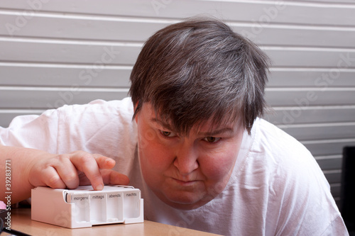 Photo: Geistig behinderte Frau mit Tablettenbox blickt traurig Geistig behinderte Frau mit Tablettenbox blickt traurig