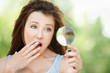 Amazed young woman looks through magnifier