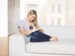 Foto: Young woman writing on notepad, sitting on sofa Young woman writing on notepad, sitting on sofa
