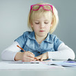 Cute child with glasses in her hairs is doing her homework