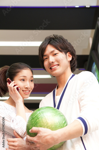Photo: ボウリング球を持つ男性とスマートフォンで話す女性 ボウリング球を持つ男性とスマートフォンで話す女性