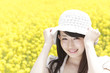 菜の花畑で帽子を被り微笑む女性