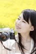 菜の花畑でカメラを持つ笑顔の女性