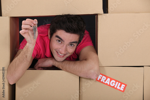 Photo: portrait of young man amid removal boxes holding key portrait of young man amid removal boxes holding key