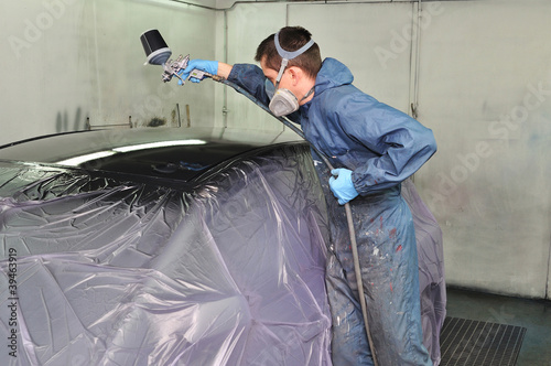 Photo: Worker painting a car roof in a paint booth. Worker painting a car roof in a paint booth.