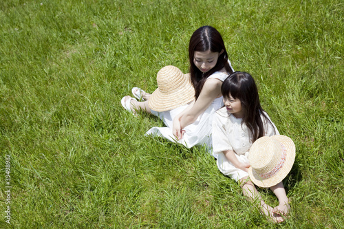 Foto: 草原に背中合わせで座る女の子と若い女性 草原に背中合わせで座る女の子と若い女性