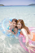 海で浮き輪に乗り手を伸ばす水着女性2人