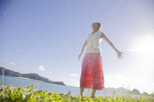 Photo: 海辺で両手を広げ太陽の光を浴びる女性 海辺で両手を広げ太陽の光を浴びる女性
