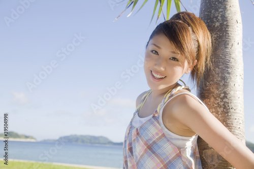 Photo: 晴天の中椰子の木に寄りかかり微笑む女性 晴天の中椰子の木に寄りかかり微笑む女性