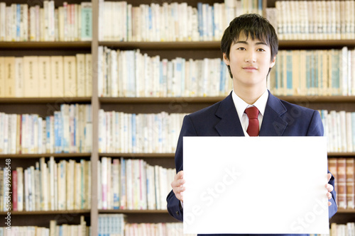Photo: 図書室でメッセージボードを持っている男子中学生 図書室でメッセージボードを持っている男子中学生