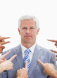 Close-up of serious businessman with fingers being pointed at him