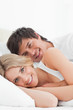 Photo: Close up, Man and woman smiling in bed embracing each other and looking forward Close up, Man and woman smiling in bed embracing each other and looking forward