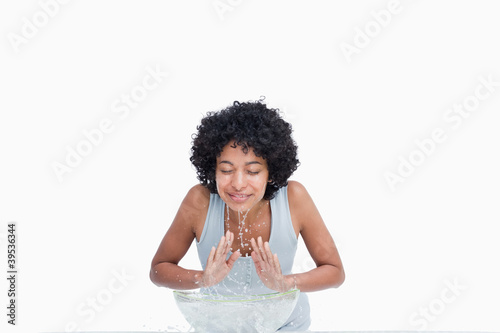 Photo: Calm young woman rinsing her face against a white background Calm young woman rinsing her face against a white background