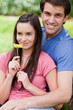 Young smiling couple standing together in the countryside with a flower