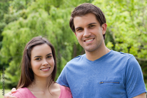 Photo: Young smiling couple standing side by side in a park Young smiling couple standing side by side in a park
