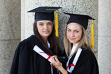 Photo: Serious graduating girl holding a digital camera while standing up with a friend Serious graduating girl holding a digital camera while standing up with a friend