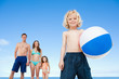 Boy with a beach ball and his family behind him on the beach