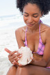 Young woman looking at a shell while sitting on the beach