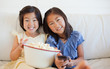 Photo: Sisters smiling on the sofa while watching tv and laughing as they enjoy popcorn Sisters smiling on the sofa while watching tv and laughing as they enjoy popcorn