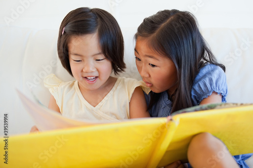 Photo: One sister turning the page as the other still reads One sister turning the page as the other still reads