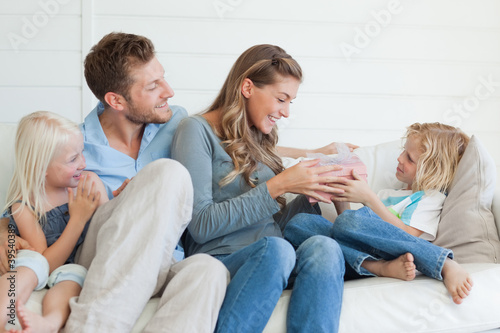 Photo: A happy family sit on the couch as the son hands his mother a present A happy family sit on the couch as the son hands his mother a present