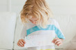 A small boy  looks at the letter to santa in his hands