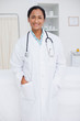 Young smiling doctor standing in a hospital room with her hands in her pockets