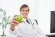 Smiling surgeon holding a green apple while sitting at the desk