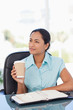Foto: Relaxed young secretary holding a cup of coffee while looking towards the side Relaxed young secretary holding a cup of coffee while looking towards the side