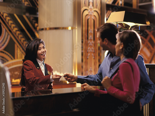Photo: Female receptionist giving room key to couple Female receptionist giving room key to couple