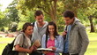 Video: Four friends laughing while pointing at a book as they stand together in a park Four friends laughing while pointing at a book as they stand together in a park
