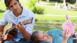 Man practises guitar as the woman rests on his leg and reads