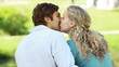A man and woman sit in the park embraced as they kiss each other