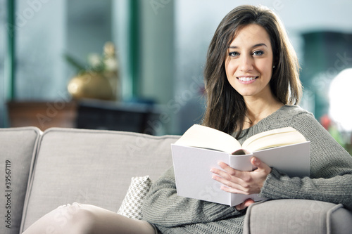 Photo: Portrait of a happy young woman lying on couch with book Portrait of a happy young woman lying on couch with book