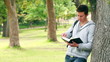 Video: Man leaning against a tree as he reads a book before looking at the camera while smiling Man leaning against a tree as he reads a book before looking at the camera while smiling