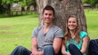 Video: Camera pans as two friends sit against a tree while smiling and looking at the camera Camera pans as two friends sit against a tree while smiling and looking at the camera