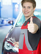 Apprentice for car mechanic in a garage shows thumb up
