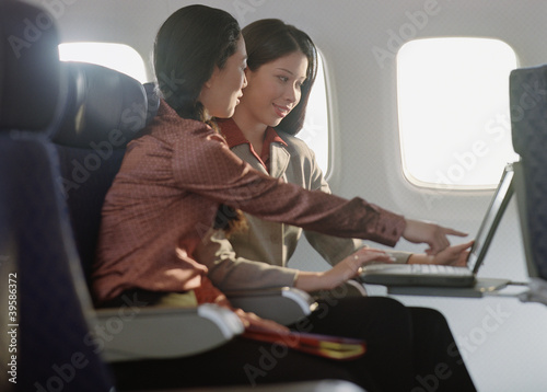 Photo: Young women using laptop on airplane Young women using laptop on airplane