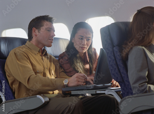 Photo: Young woman and man using laptop on airplane Young woman and man using laptop on airplane